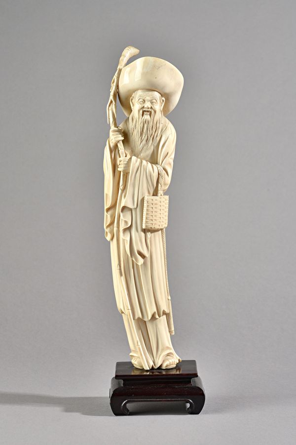 A Chinese ivory figure of an elderly man, late 19th/early 20th century, standing in long robes wearing a hat, carrying a bag  under his left arm and h