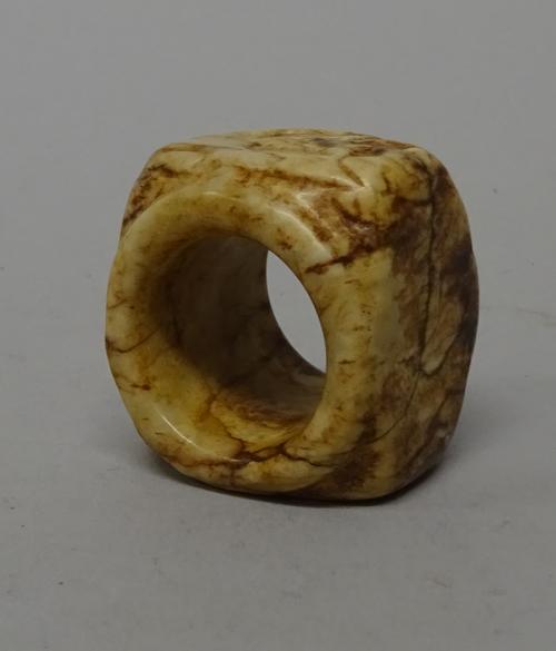 A Chinese cream and brown jade cong, probably 4th century B.C, rounded square form with tubular centre, carved on one side of the exterior with  mythi