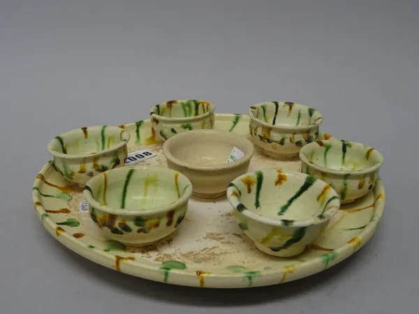 A Chinese circular pottery tray and six cups, Tang dynasty, each piece splashed in green and ochre, tray 24.5cm. diameter; and an unglazed U-shaped cu