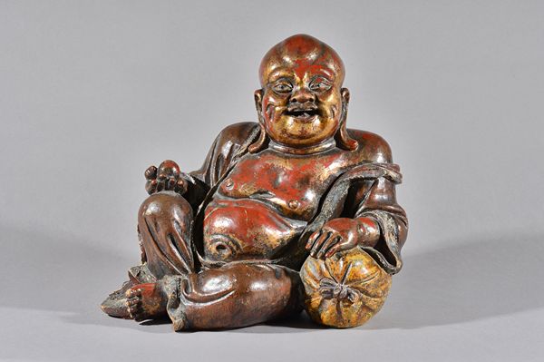 A large Chinese lacquered and gilt wooden figure of Budai, 19th century, carved seated and leaning against a sack, 33cm. high.