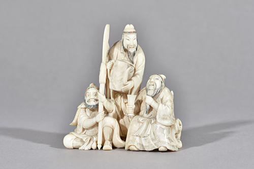 A Japanese ivory okimono, Meiji period, carved as a man standing about to pour tea to a seated official, a grimacing warrior seated beside holding a h