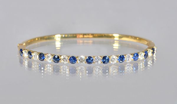 An 18ct gold, sapphire and diamond oval hinged bangle, claw set with a row of circular cut diamonds alternating with circular cut sapphires, on a snap