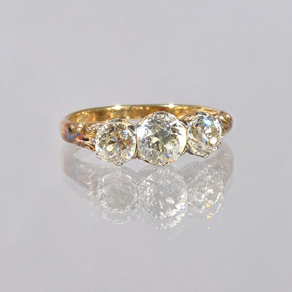 A gold and diamond set three stone ring, claw set with a row of cushion shaped diamonds and with the principal diamond mounted at the centre, the moun