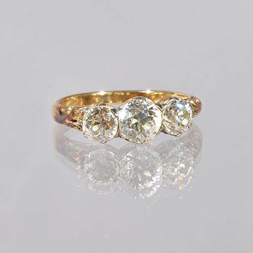 A gold and diamond set three stone ring, claw set with a row of cushion shaped diamonds and with the principal diamond mounted at the centre, the moun