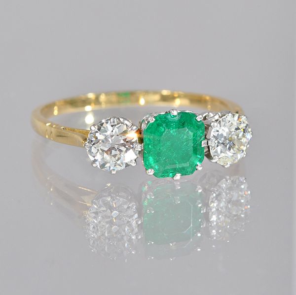 A gold, emerald and diamond set three stone ring, claw set with the cut cornered square step cut emerald to the centre, between two claw set cushion s