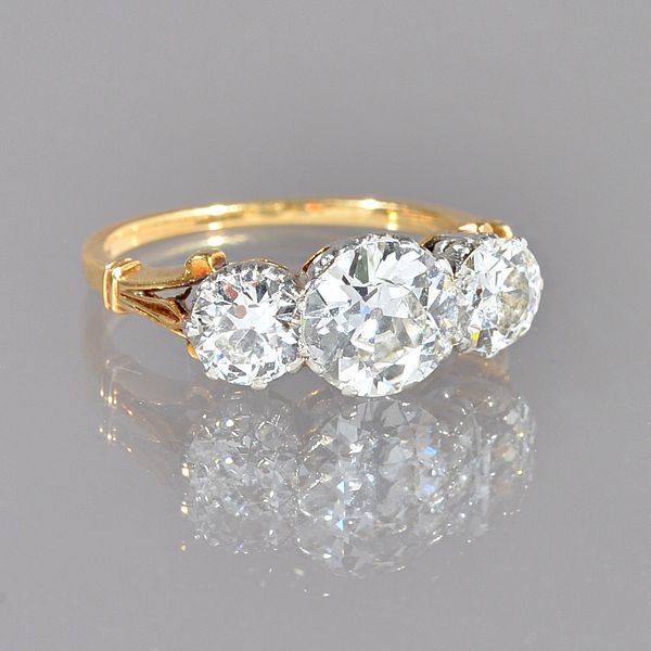 A gold and diamond three stone ring, claw set with the principal cushion shaped diamond to the centre, between two smaller cushion shaped diamonds, be