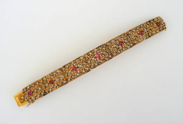 A gold, ruby and diamond bracelet, formed as a row of curved rectangular panel shaped links, each centred by a cabochon ruby and otherwise mounted wit