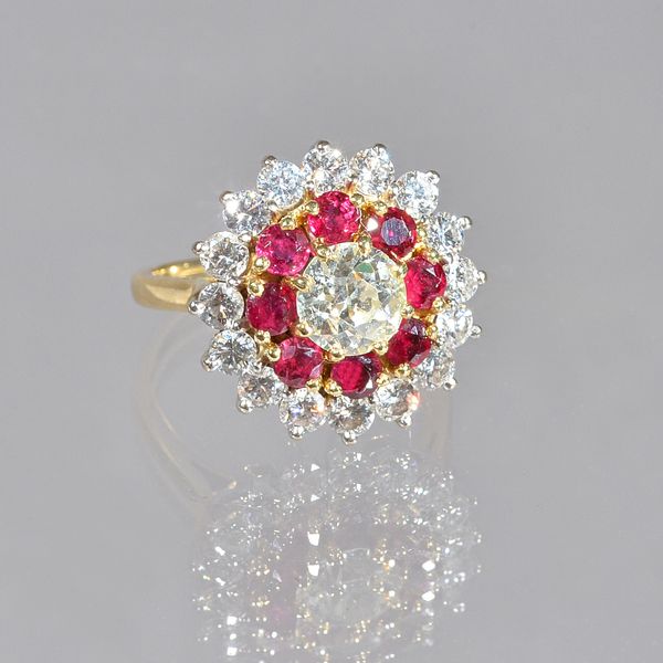 An 18ct gold, diamond and ruby cluster ring, claw set with the principal cushion shaped diamond at the centre, in a surround of eight circular cut rub