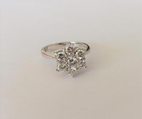 An 18ct white gold and diamond seven stone cluster ring, claw set with circular cut diamonds, ring size N and a half, with a case and a box.
