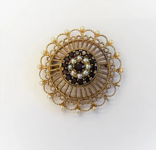 A 9ct gold, garnet and cultured pearl pendant brooch, in a shaped circular wirework design, claw set with the principal circular cut garnet to the cen