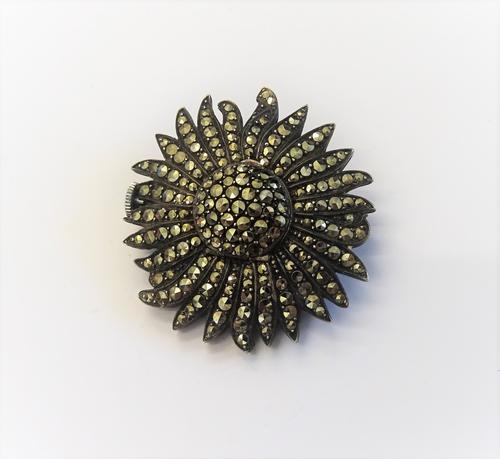 A silver and marcasite set brooch watch, designed as a single flowerhead, the centre opening to reveal a watch compartment, the silvered dial with bla