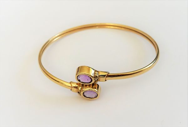 A 9ct gold and amethyst bangle, collet set with two oval cut amethysts, in a twistover design, gross weight 6.8 gms.