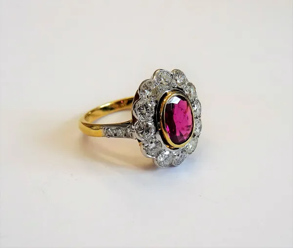 A gold, ruby and diamond oval cluster ring, collet set with the oval cut ruby at the centre in a surround of twelve circular cut diamonds, between dia