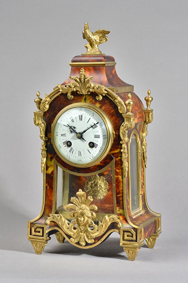 A FRENCH ORMOLU-MOUNTED TORTOISESHELL MANTEL CLOCKIn the Regence style, circa 1910The case surmounted by a cockerel, above an arch with convex glazed