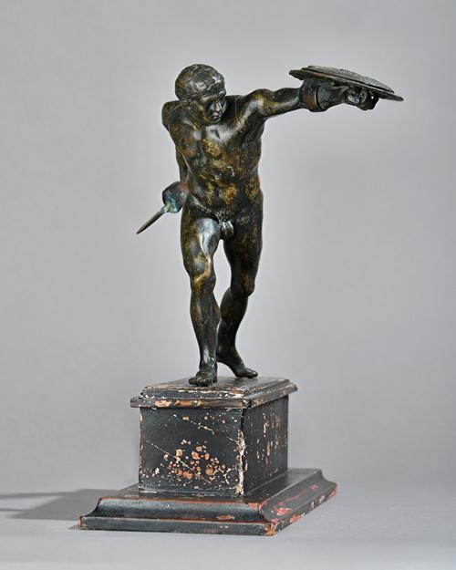 An early 19th century patinated bronze 'Gladiator' figure, modelled with sword and shield on top of a distressed ebonised wooden base, 31.5cm high, (2