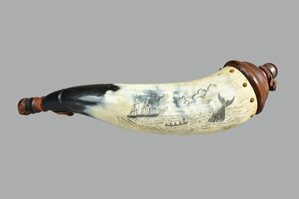 A mid-19th century scrimshaw cow horn powder flask, detailed in black ink with a whale hunting scene and with turned  wooden finials united by a leath