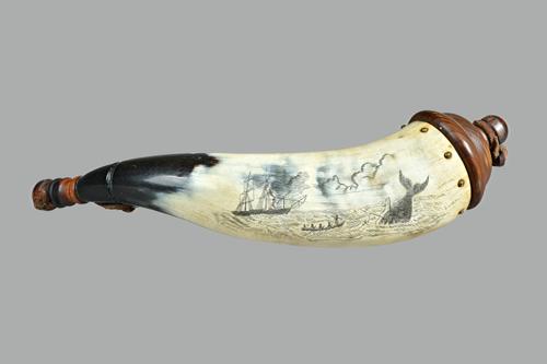 A mid-19th century scrimshaw cow horn powder flask, detailed in black ink with a whale hunting scene and with turned  wooden finials united by a leath