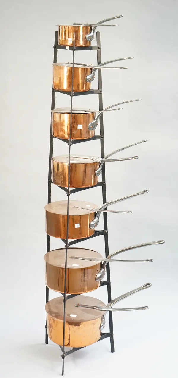 A graduated set of seven copper saucepans and lids, late 19th century, with a later wrought iron storage rack, 146cm high.