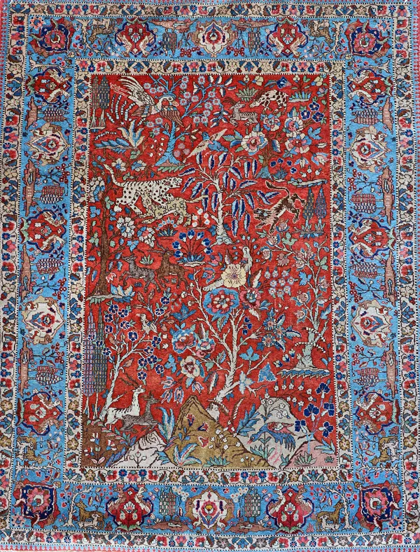 A Tabriz rug, Persian, the madder field with a landscape of hills and trees, tigers, lions, birds and deer, an indigo palmette and cartouche border wi