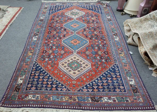 A Shiraz rug, Persian, the madder field with two indigo and two fawn connecting medallions, indigo spandrels, all with floral sprays, a fawn stylised