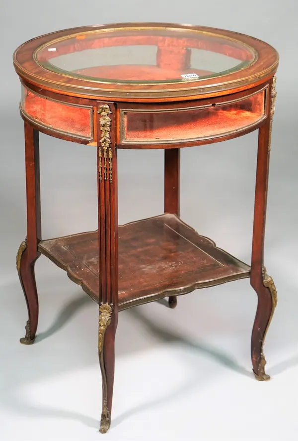 A Louis XVI style gilt metal mounted mahogany vertu table, the glazed lift circular top and sides on four channelled supports, united by  platform und