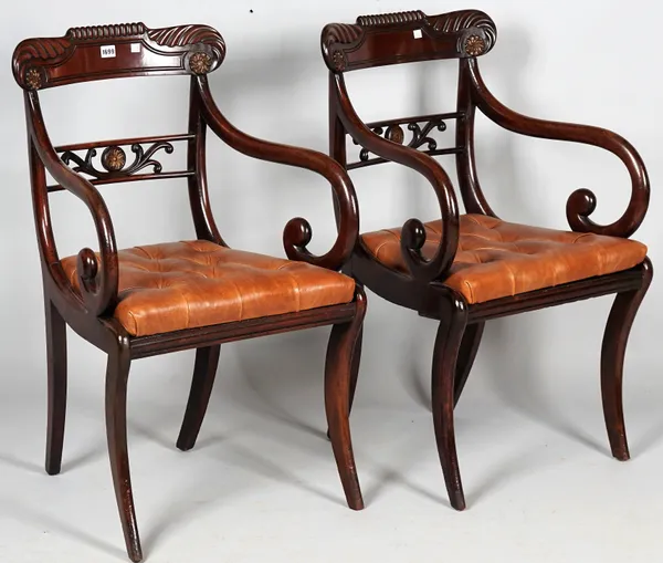 A pair of Regency mahogany carver chairs with parcel gilt floral motif crest over pierced waist rail, on sabre supports, 54cm wide x 88cm high.