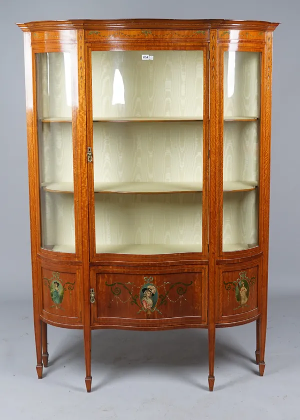 An Edwardian polychrome painted satinwood display cabinet, the serpentine front with glazed door over cupboard, on tapering square supports, 128cm wid