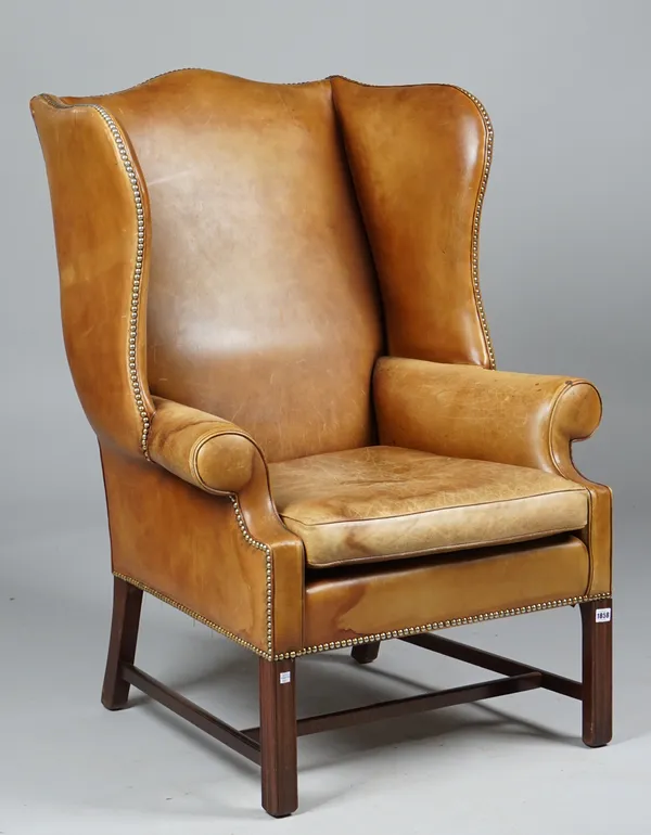 A George III style tan leather upholstered wingback armchair on block mahogany supports, 80cm wide x 114cm high.