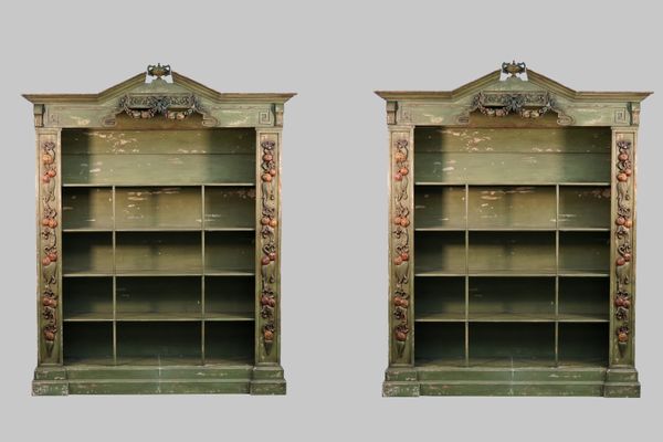 A pair of Baroque revival green painted floor standing open bookcases, the urn mounted broken architectural cornice with polychrome fruiting swags on