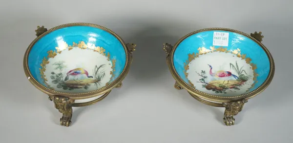 A matched pair of Sevres-style gilt metal mounted saucers, 19th century, each painted with a bird in a landscape inside a gilt foliate frame against a