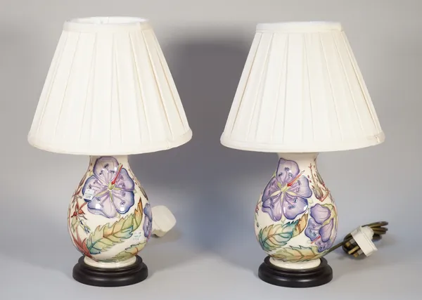 A pair of Moorcroft Pottery table lamps, tube line decorated with hibiscus against a cream ground, each on a wooden base with cream pleated shade, 40c