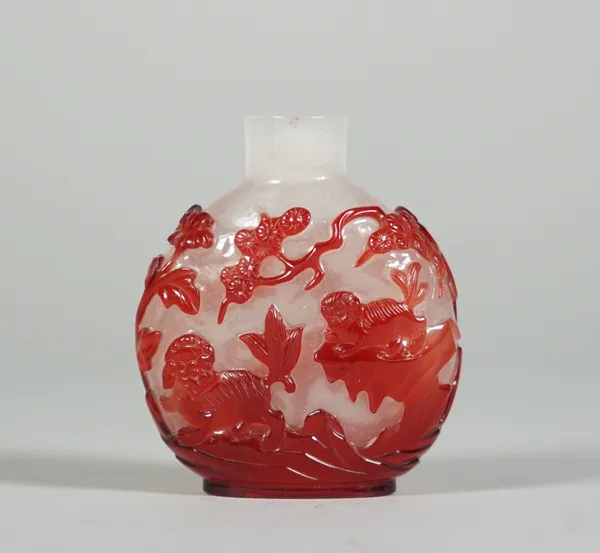 A Chinese red overlay glass snuff bottle, 19th century, carved on one side with a Buddhist lion and cub in a landscape, the reverse with a bird flanke