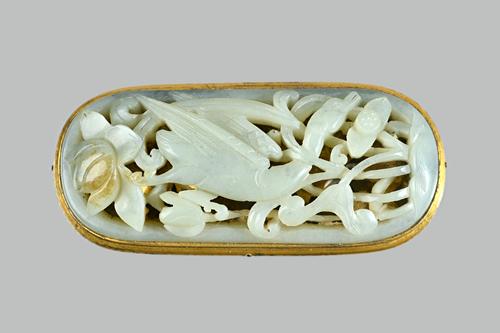 A Chinese celadon jade plaque, probably 17th/18th century, set with a gilt-metal mount, carved and pierced with a bird amongst lotus, the stone with b