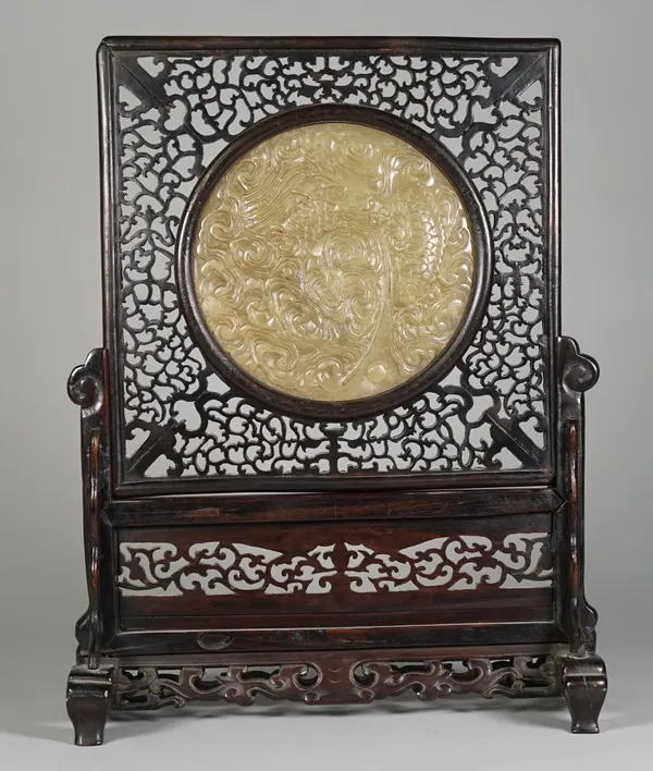 A Chinese wooden table screen with inset bowenite panel, late 19th/early 20th century, the circular panel carved with a coiled dragon chasing a flamin