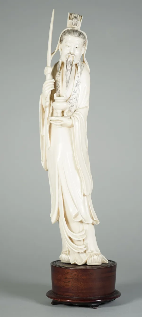 A Chinese ivory figure of a sage, early 20th century, standing in long robes carrying a ceremonial sword and a censer, 31cm. high, wood stand.