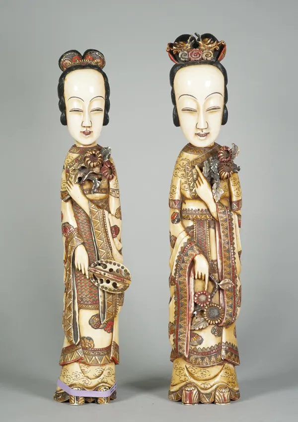 A pair of Chinese ivory figures of a mother and daughter, early 20th century, carved and painted standing in long robes, each holding flowers, the dau