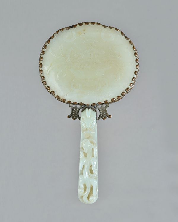 A Chinese jade and gilt-metal mounted hand mirror, 19th century, the handle formed as a pale celadon belt hook, carved with a chilong crawling towards