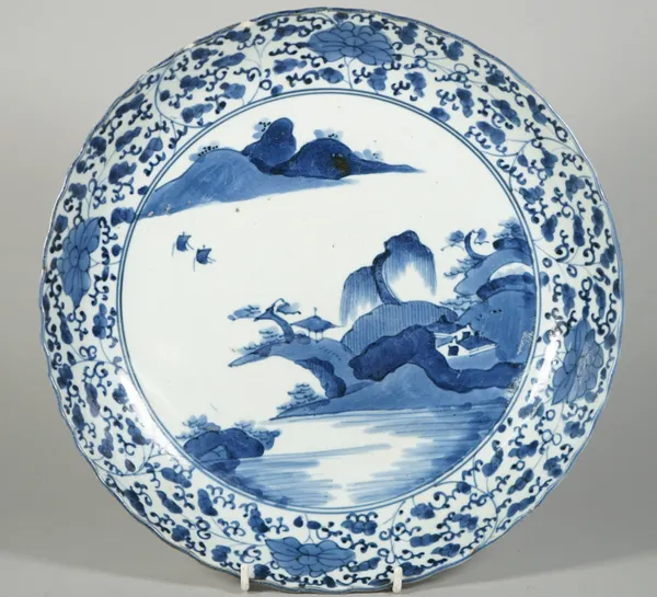 An Arita blue and white dish, Edo period, 18th century, painted with a river landscape beneath a border filled with flowers and tendrils, (a.f), 31.5c