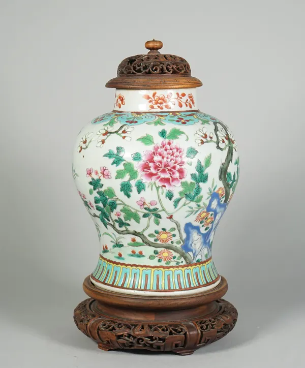 A Chinese famille-rose baluster vase, late 19th century, brightly enamelled with flowering shrubs and pierced blue rocks, 21cm. high, pierced wood cov
