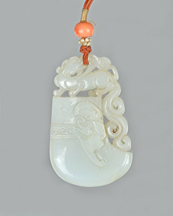 A Chinese white jade pendant, Qing dynasty, in the form of an archaistic axe, carved on the front with a bat and surmounted by a horned beast with a s