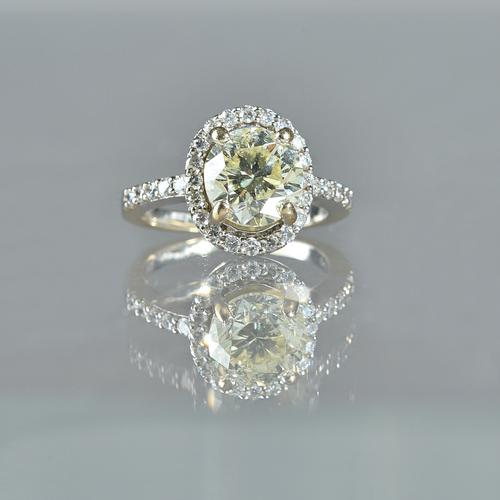 An 18ct white gold and diamond ring, claw set with the principal circular cut diamond to the centre, in an oval surround, set with smaller circular cu