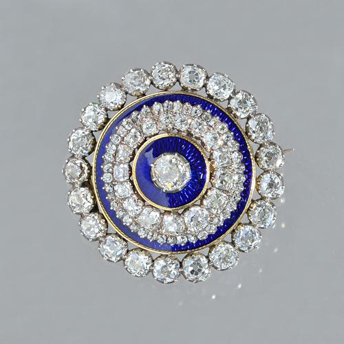 A gold backed and silver set diamond and blue enamelled brooch, of circular form, mounted with the principal cushion shaped diamond to the centre, on