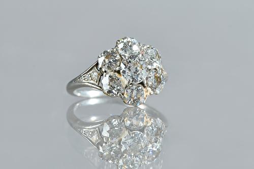 A diamond set seven stone cluster ring, claw set with the principal cushion shaped diamond to the centre, in a surround of six smaller cushion shaped