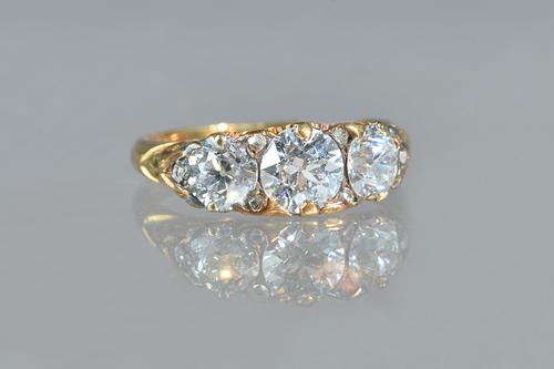 A gold and diamond three stone ring, claw set with a row of cushion shaped diamonds and with the principal diamond mounted at the centre, further set