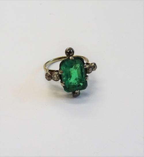 An emerald and diamond ring, claw set with the cut cornered rectangular step cut emerald to the centre, between two pairs of cushion shaped diamonds a
