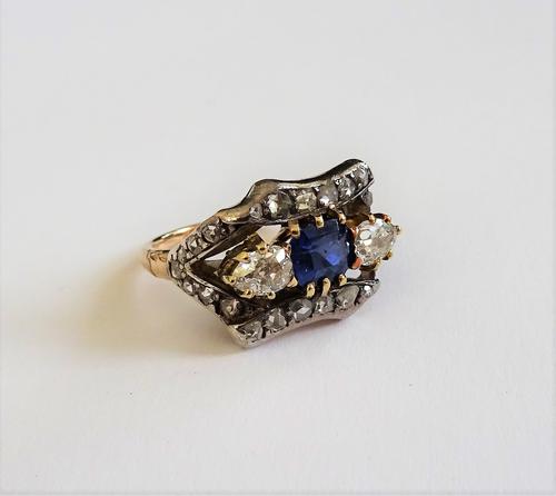A gold and silver set, sapphire and diamond ring, claw set with the cushion cut sapphire to the centre, between two pear shaped diamonds within an ope