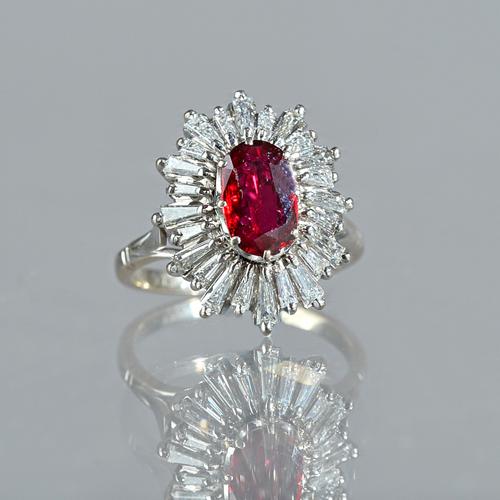 A white gold, ruby and diamond set shaped oval cluster ring, claw set with the oval cut ruby at the centre, within a surround of tapered baguette diam