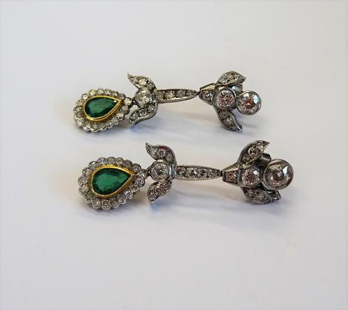 A pair of diamond and emerald pendant earrings, each with an associated drop, collet set with a pear shaped emerald at the centre, in a surround of ci