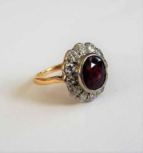 A gold, ruby and diamond set oval cluster ring, collet set with the oval cut ruby at the centre, in a surround of twelve circular cut diamonds, ring s