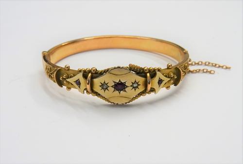 A 9ct gold, ruby and rose diamond set oval hinged bangle, star set with the principal cushion shaped ruby at the centre, between two rose diamonds, ot